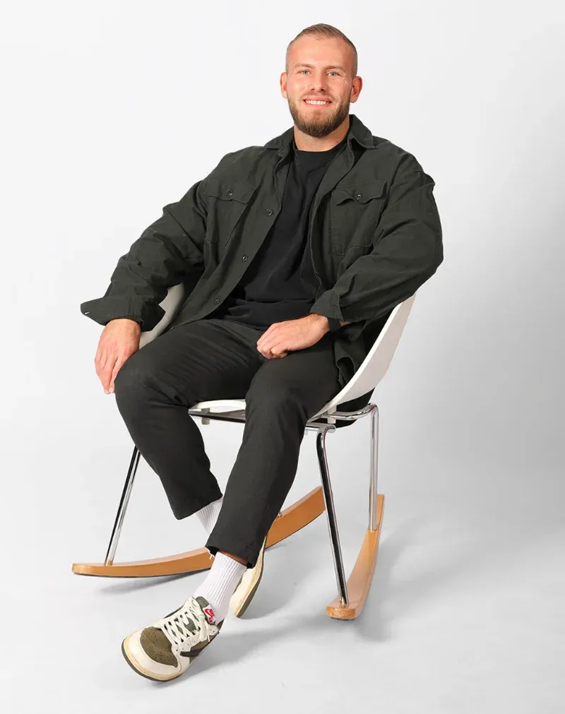 Nick Martin, Geschäftsführender Gesellschafter von amplifyy, sitzt lächelnd in dunkler Hemdjacke auf einem weißen Schaukelstuhl vor hellem Hintergrund